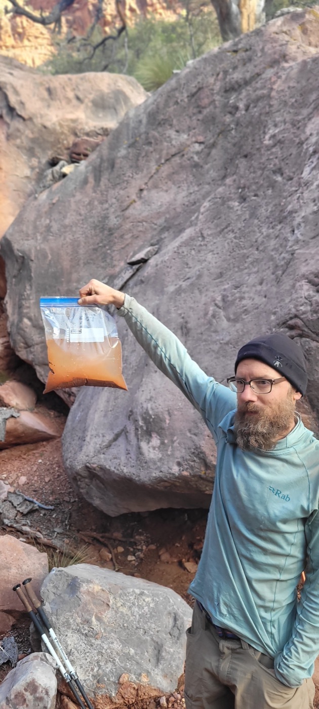 Hiker holding a ziplock bag of orange-red muddy water in the Grand Canyon